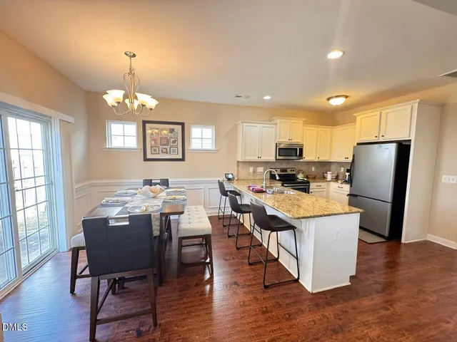 an open kitchen with granite countertop a refrigerator a stove a sink a dining table and chairs with wooden floor