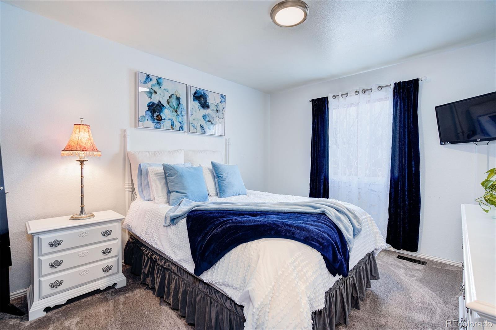 612 Ruby Drive Fort Collins, CO 80525 - Photo 19 of 40 a bedroom with a bed a lamp and a flat screen tv