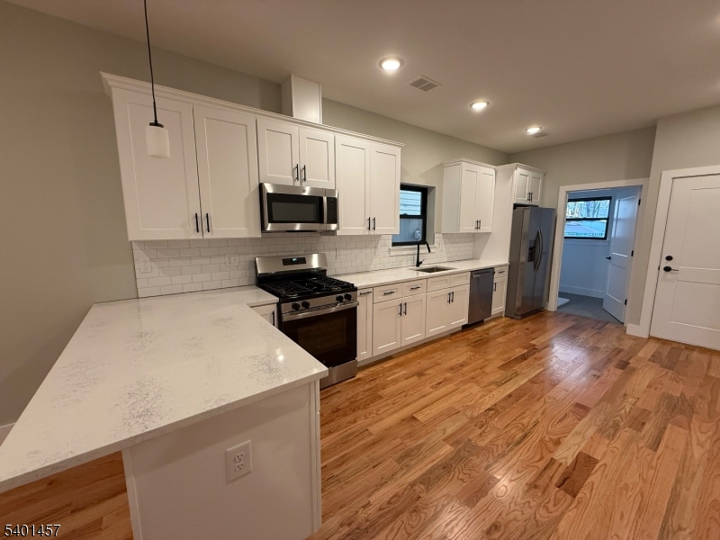 76 Barbara Street, Unit 1 Newark, NJ 07105 - Photo 5 of 8 a kitchen with stainless steel appliances a stove top oven a sink a refrigerator white cabinets and wooden floor