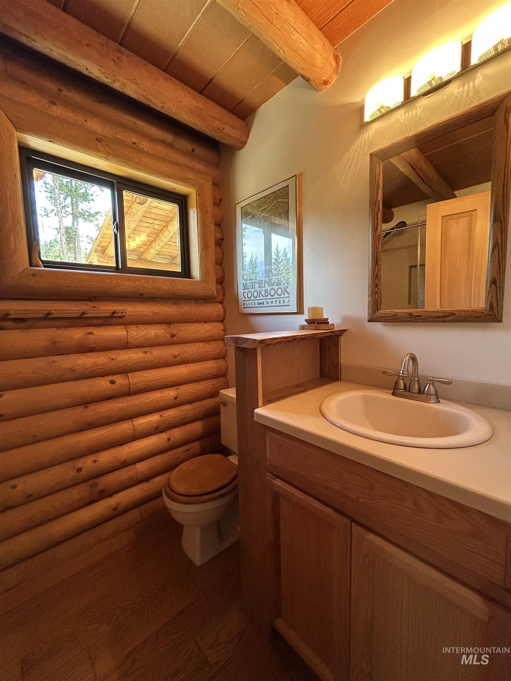 35 Sawtooth Way Stanley, ID 83278 - Photo 22 of 36 Rustic bathroom featuring log walls, wood-finish flooring, a single vanity with a light-toned countertop, and a framed mirror