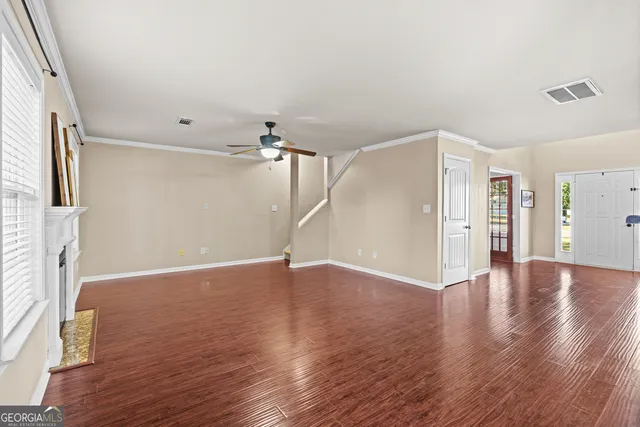 a view of an empty room with wooden floor and a ceiling fan