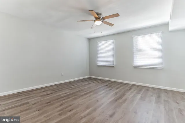 an empty room with wooden floor windows and fan