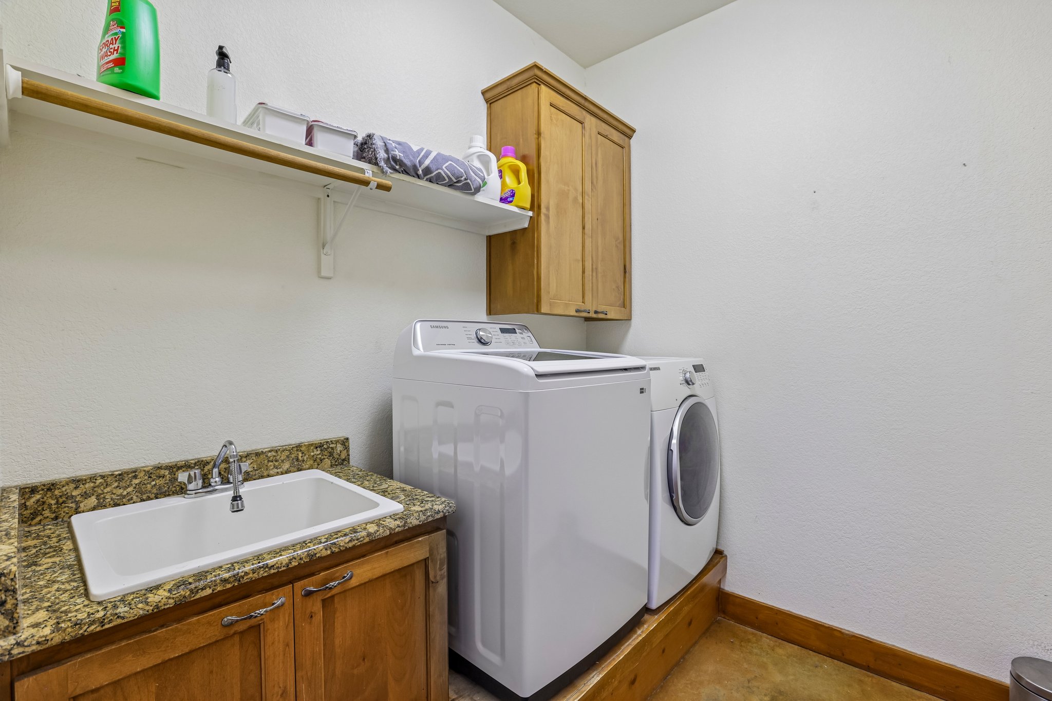 267 Corral Road Smithville, TX 78957 - Photo 25 of 40 Dedicated laundry area featuring a utility sink with a granite-style countertop, wood-finish cabinetry, and overhead shelving