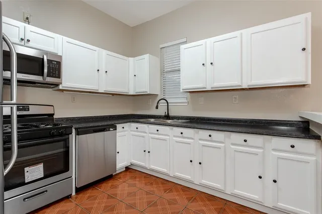 a kitchen with granite countertop white cabinets stainless steel appliances and wooden floor