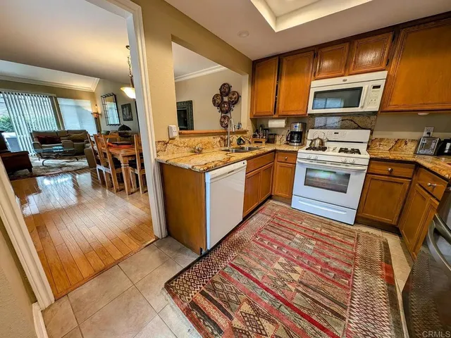 a kitchen with stainless steel appliances granite countertop a stove top oven a sink dishwasher a dining table and chairs with wooden floor