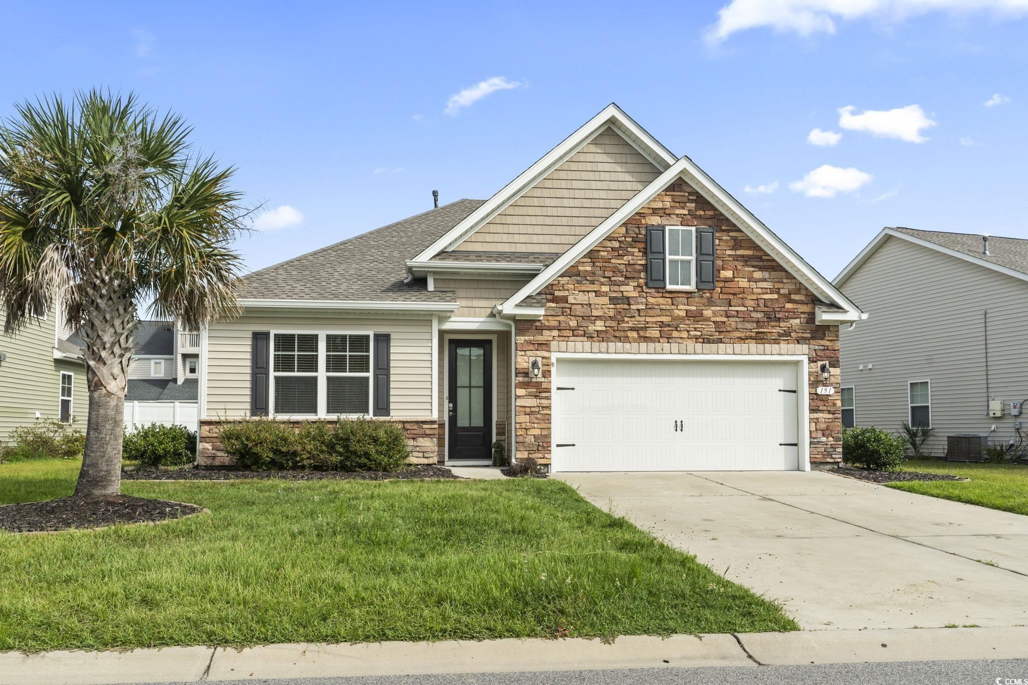 Craftsman house featuring stone siding, a front yard, driveway, a shingled roof, and a garage