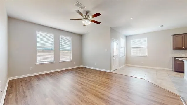 an empty room with wooden floor chandelier fan and windows