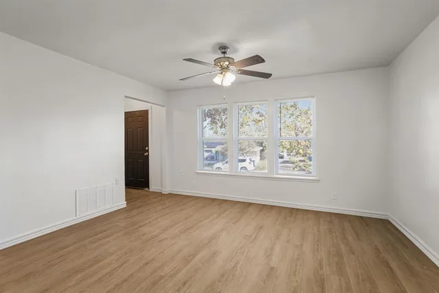 an empty room with wooden floor chandelier fan and windows