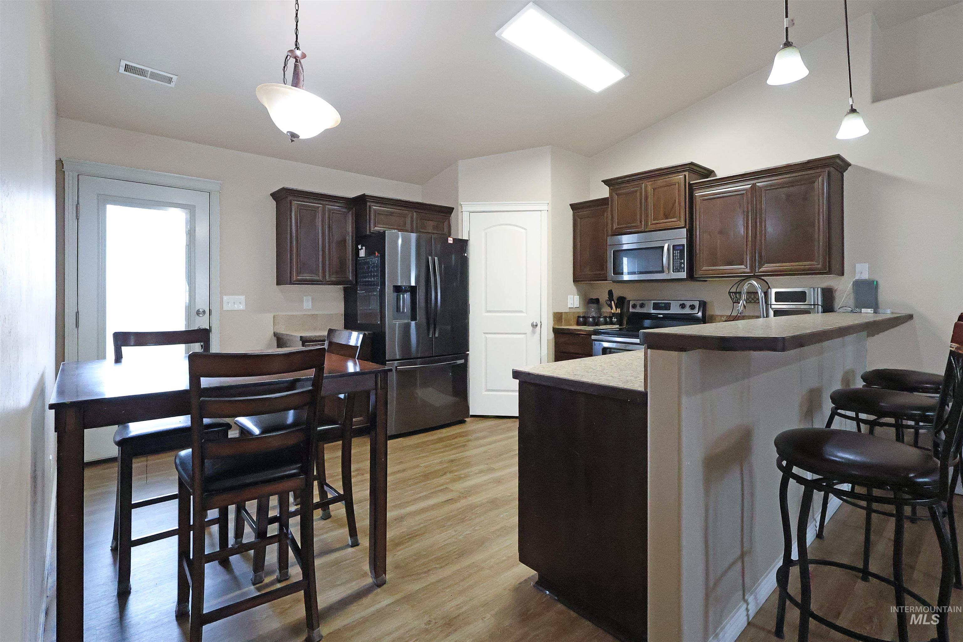 717 South B Street Rupert, ID 83350 - Photo 5 of 13 Kitchen featuring dark brown cabinets, appliances with stainless steel finishes, lofted ceiling, a breakfast bar area, and decorative light fixtures