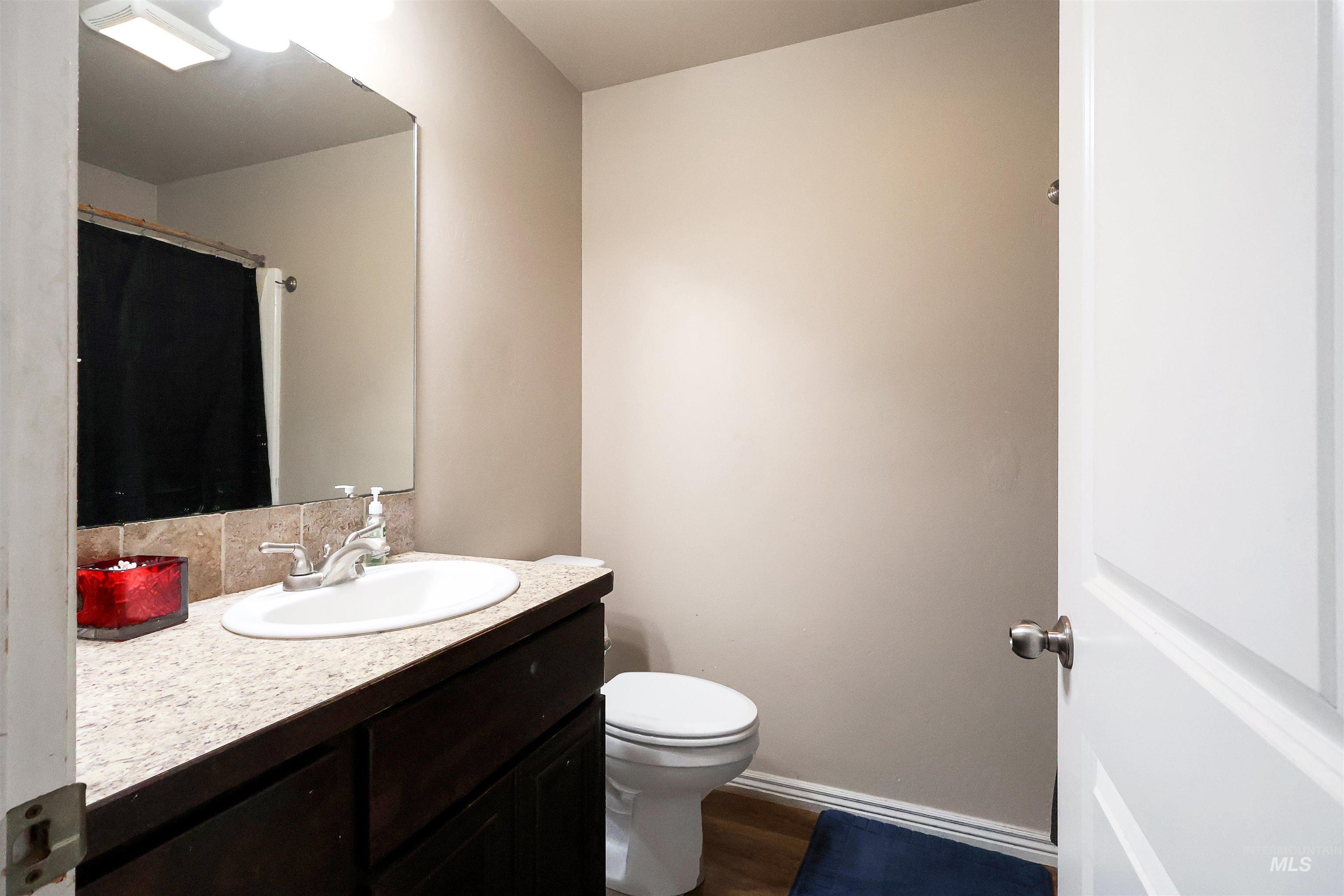 717 South B Street Rupert, ID 83350 - Photo 10 of 13 Full bathroom featuring vanity, curtained shower, dark wood-style flooring, and decorative backsplash