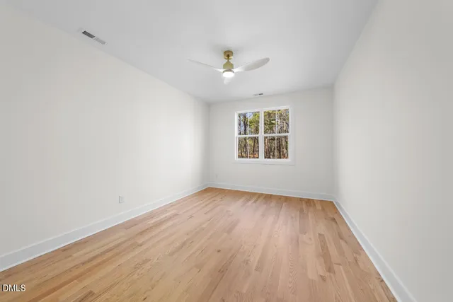 an empty room with wooden floor ceiling fan and windows