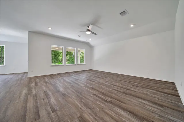 an empty room with wooden floor ceiling fan and windows