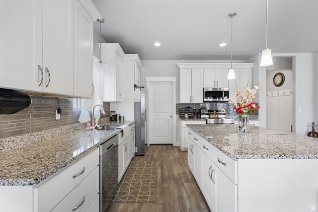 7889 Bristlecone Road Eagle Mountain, UT 84005 - Photo 12 of 42 Bright kitchen featuring white cabinetry, wood-finish flooring, stainless steel appliances, a tile backsplash, and speckled countertops