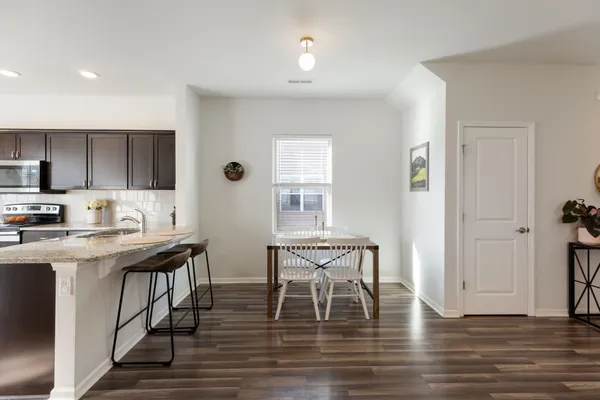 a kitchen with stainless steel appliances granite countertop a stove top oven a sink a dining table and chairs with wooden floor
