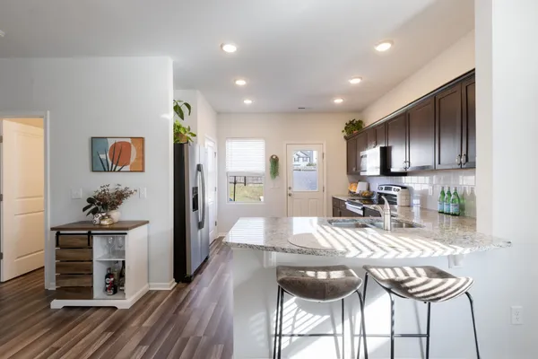 a kitchen with granite countertop kitchen island stainless steel appliances a stove a refrigerator a stove a sink a dining table and chairs with wooden floor