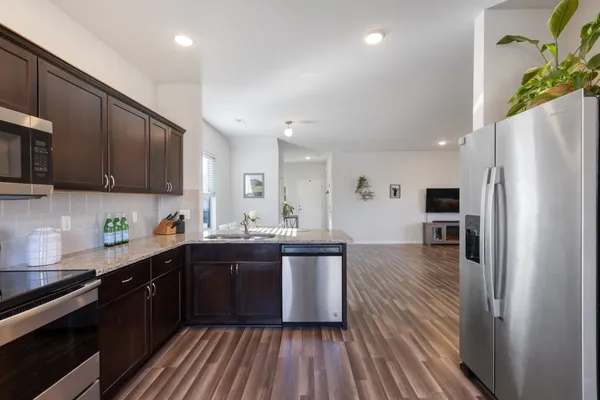 a kitchen with stainless steel appliances granite countertop a refrigerator a sink dishwasher a stove and white countertops with wooden floor