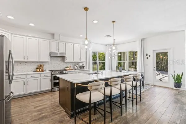 a kitchen with stainless steel appliances a dining table chairs stove refrigerator and cabinets