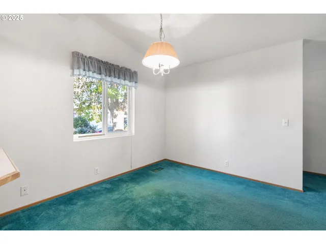 a view of an empty room with window and chandelier fan
