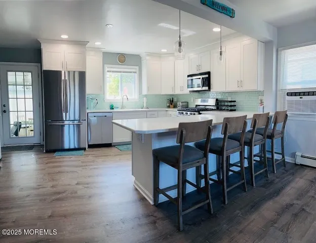 a kitchen with stainless steel appliances granite countertop a stove a refrigerator a kitchen island a dining table and chairs with wooden floor