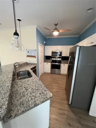 a kitchen with stainless steel appliances granite countertop a refrigerator a sink and white cabinets with wooden floor