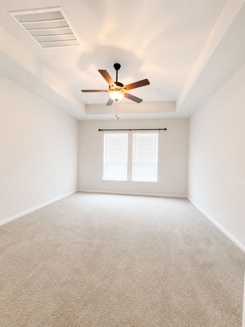 693 Durian Loop Buda, TX 78610 - Photo 14 of 27 A spacious, naturally illuminated room presents soft carpeting and a ceiling fan, promising comfort and serenity.