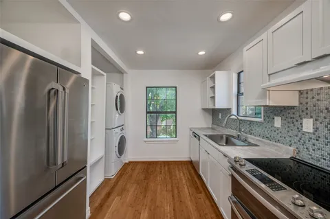 a kitchen with stainless steel appliances granite countertop a refrigerator a sink dishwasher a stove and white countertops with wooden floor