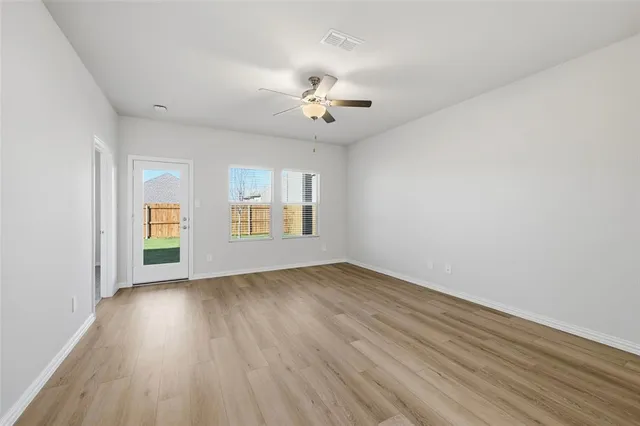 an empty room with wooden floor chandelier fan and windows