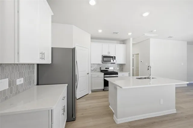 a kitchen with stainless steel appliances a sink stove refrigerator and white cabinets with wooden floor