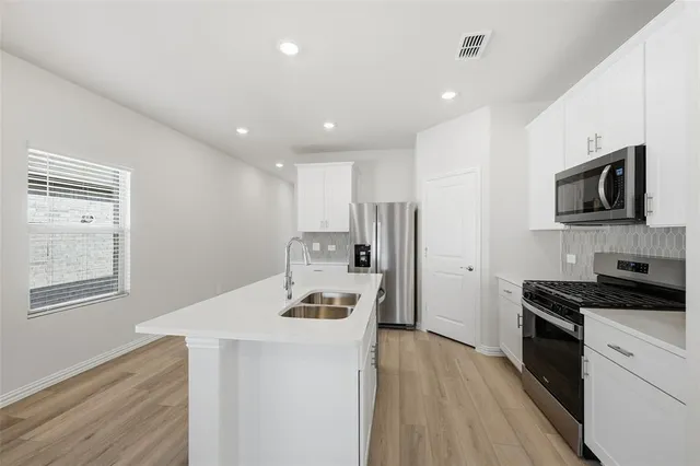 a kitchen with stainless steel appliances a stove a refrigerator a sink dishwasher and a stove with wooden floor