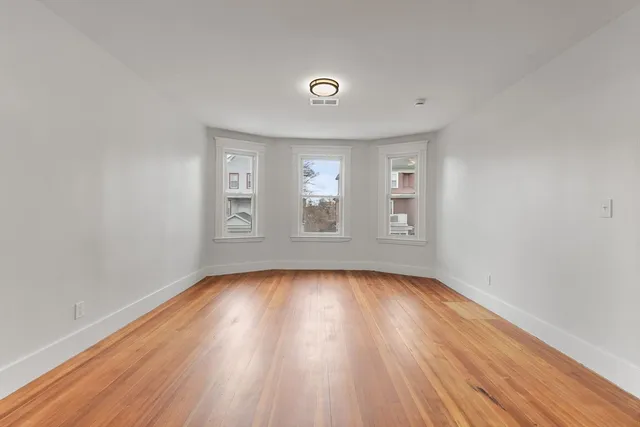 a view of an empty room with wooden floor and window