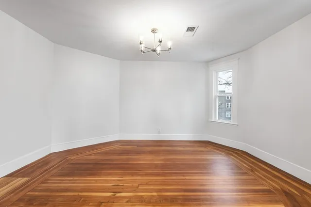 an empty room with wooden floor chandelier and windows