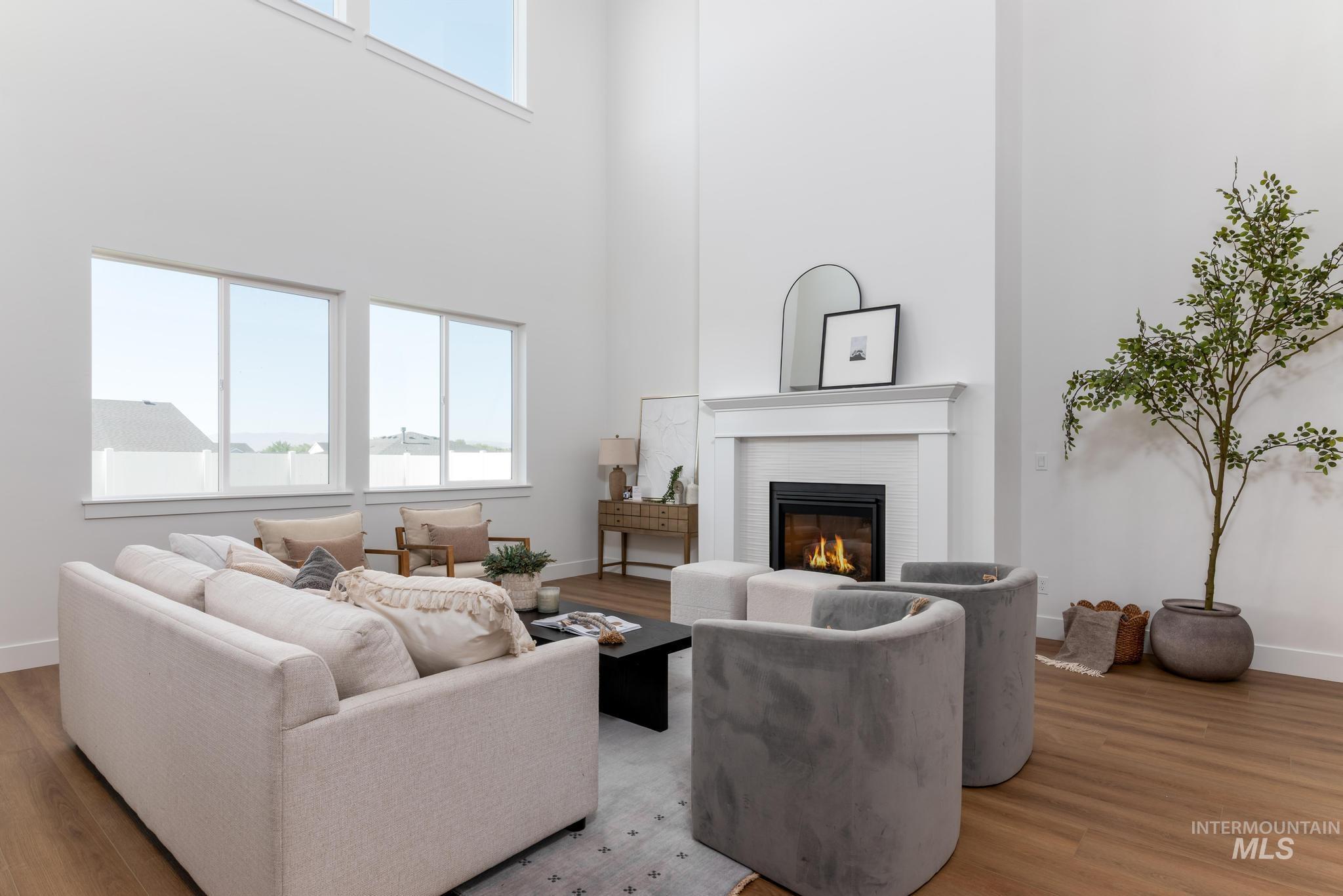 14703 Serenity Pt Street Caldwell, ID 83607 - Photo 6 of 45 Two-story living area featuring a fireplace with white mantel, wood-finish flooring, high ceilings, and tall windows