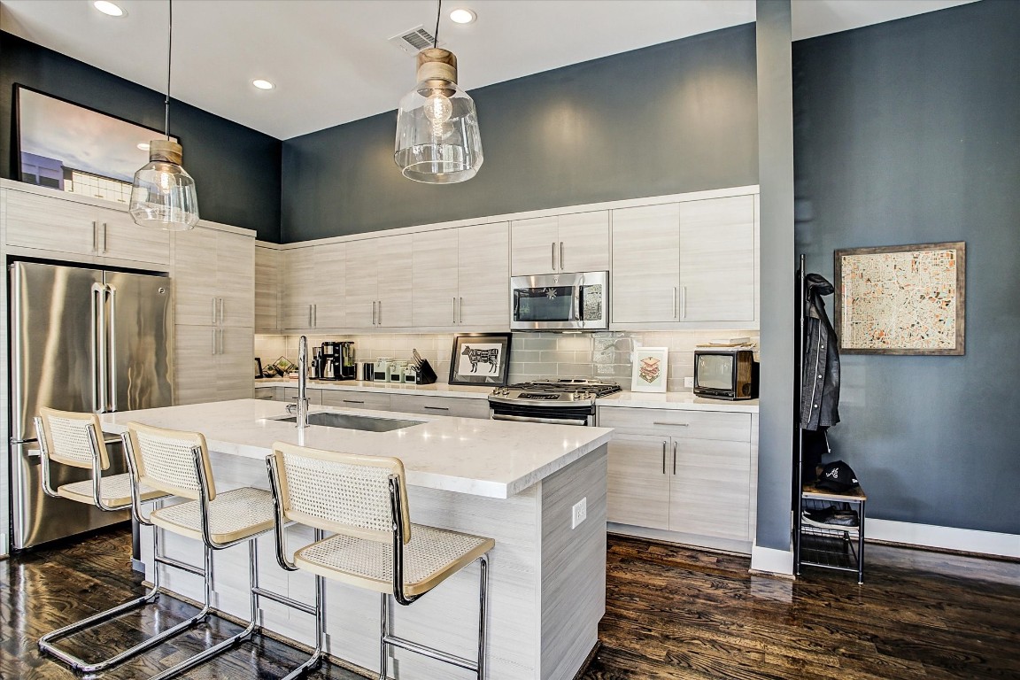 1004 California Street, Unit 101 Houston, TX 77006 - Photo 8 of 27 a kitchen with stainless steel appliances kitchen island granite countertop a stove a refrigerator a sink dishwasher a dining table and chairs with wooden floor