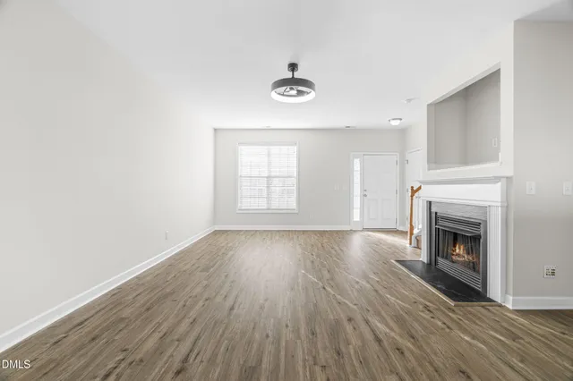 a view of an empty room with wooden floor fireplace and a window