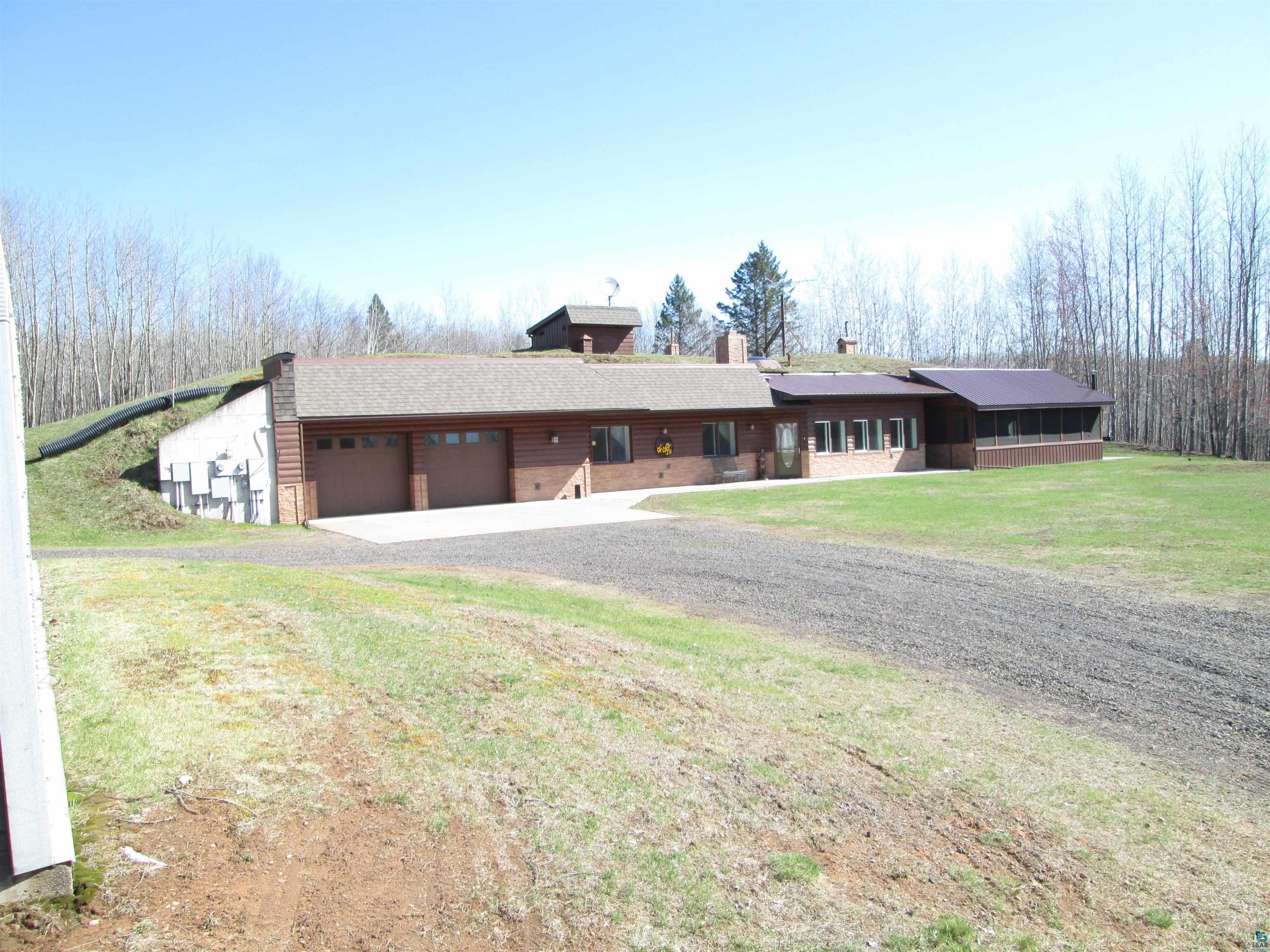 View of front of home with an attached garage, a chimney, a front yard, and gravel driveway