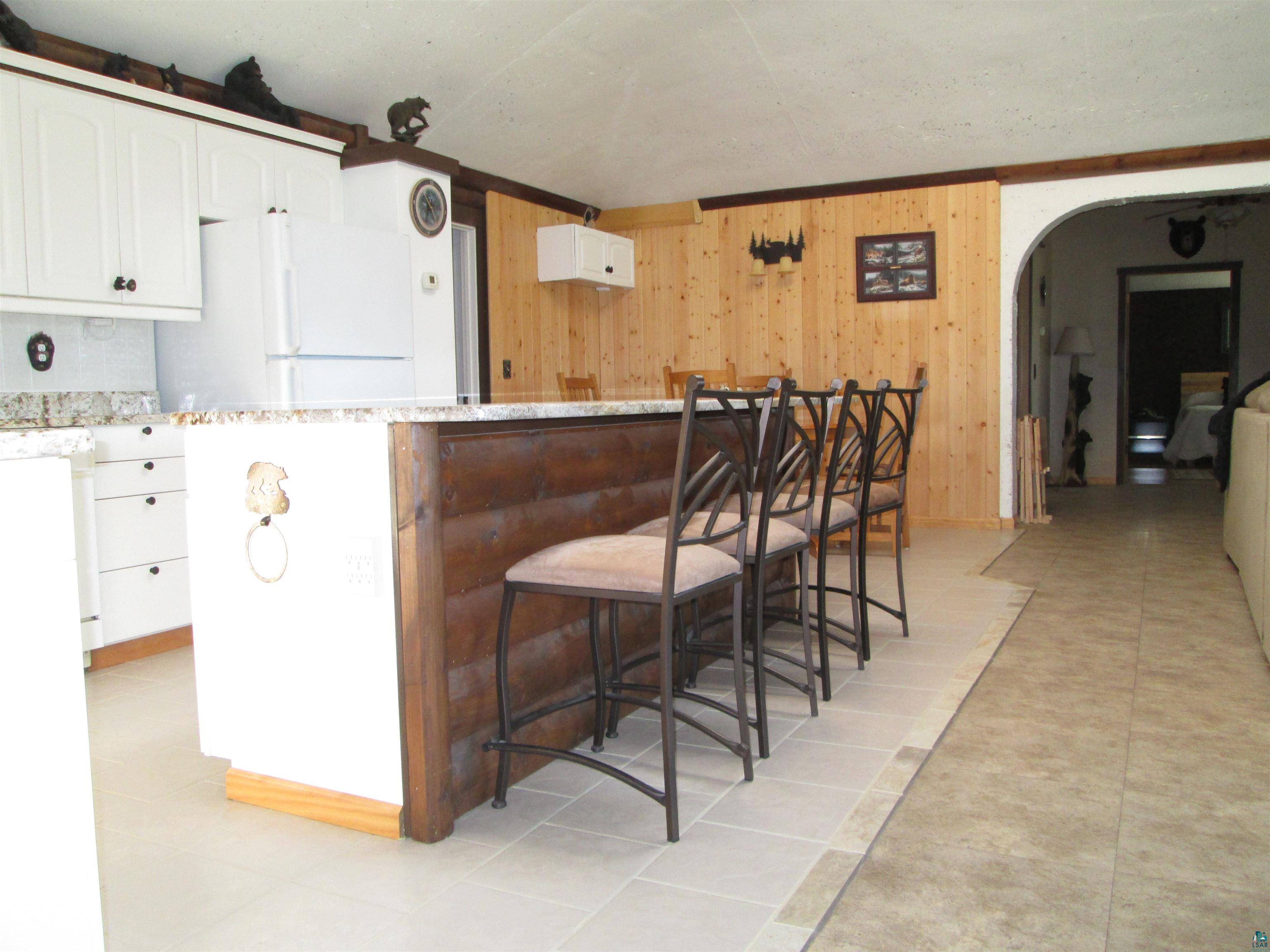 8882 Shortcut Road Lake Nebagamon, WI 54849 - Photo 11 of 47 Kitchen with freestanding refrigerator, a breakfast bar area, wooden walls, white cabinetry, and arched walkways