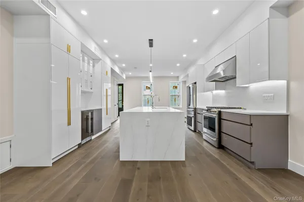 a large white kitchen with stainless steel appliances granite countertop a stove oven a refrigerator and white cabinets with wooden floors