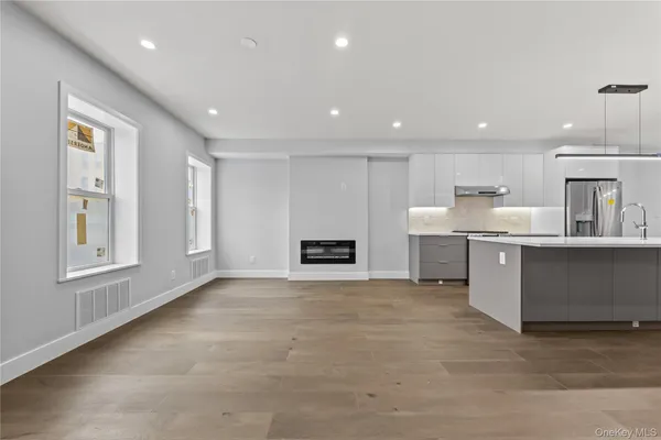 a large white kitchen with stainless steel appliances granite countertop a stove a sink a refrigerator and white cabinets with wooden floor