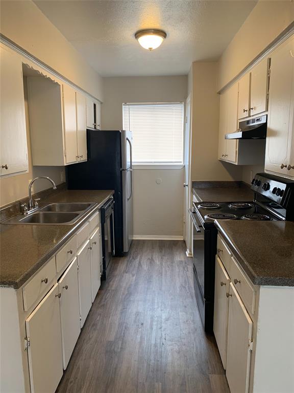 4606 Monarch Street, Unit 109 Dallas, TX 75204 - Photo 10 of 17 Kitchen with black appliances, dark countertops, under cabinet range hood, dark wood-style floors, and a textured ceiling