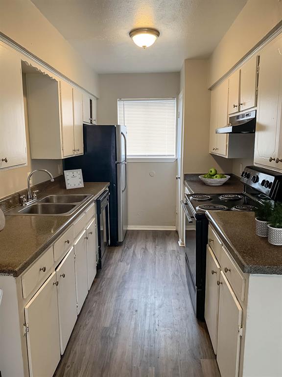 4606 Monarch Street, Unit 109 Dallas, TX 75204 - Photo 5 of 17 Kitchen with black appliances, dark countertops, under cabinet range hood, dark wood-style flooring, and a textured ceiling