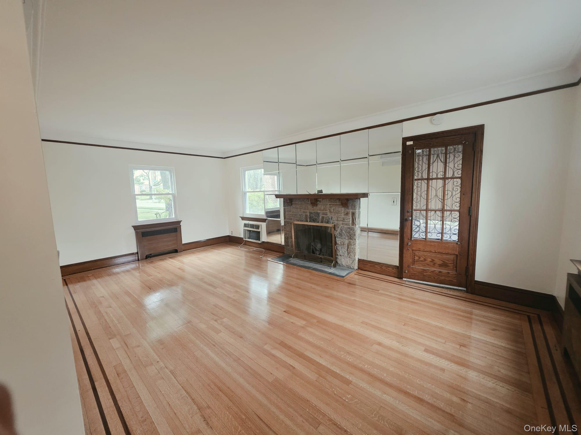 180-15 Dalny Road Queens, NY 11432 - Photo 2 of 10 an empty room with windows fireplace and wooden floor