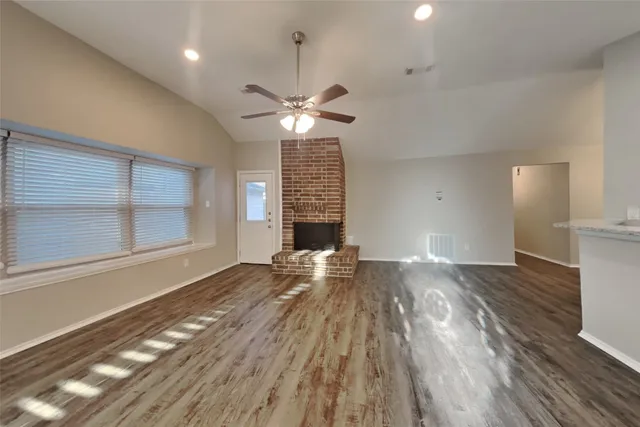 a view of an empty room with wooden floor fireplace and a window