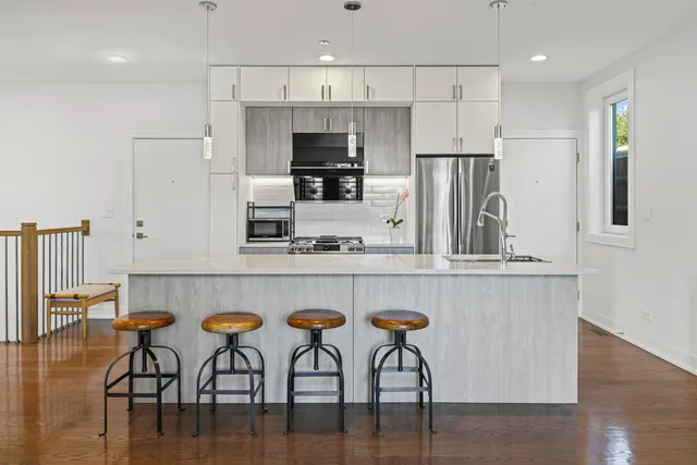 a kitchen with stainless steel appliances a dining table chairs refrigerator and microwave