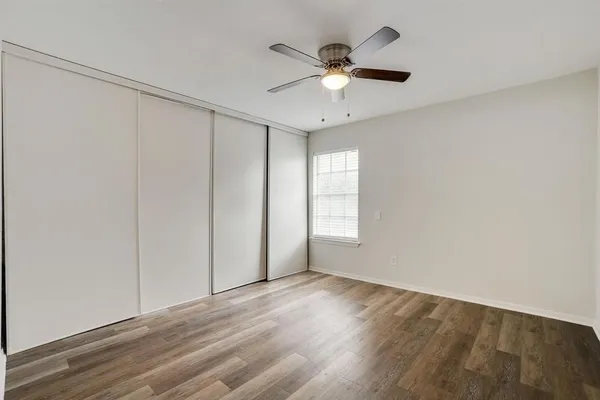 an empty room with wooden floor fan and windows