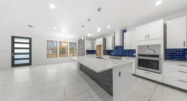 a large white kitchen with kitchen island granite countertop a stove a oven a sink and white cabinets