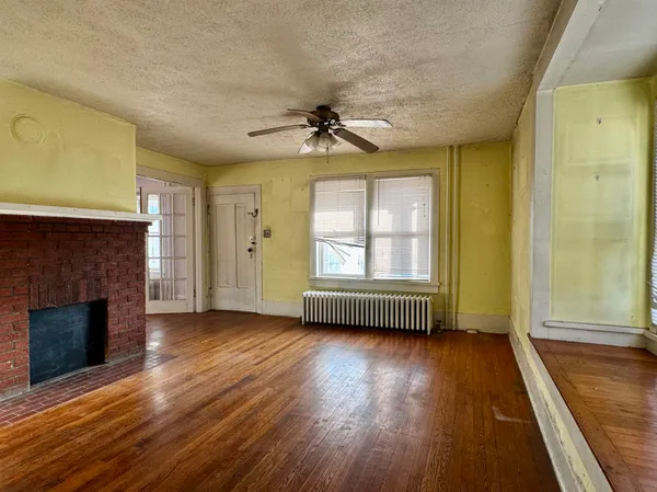 an empty room with wooden floor fireplace and windows
