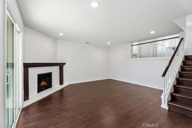 a view of an empty room with wooden floor fireplace and a window
