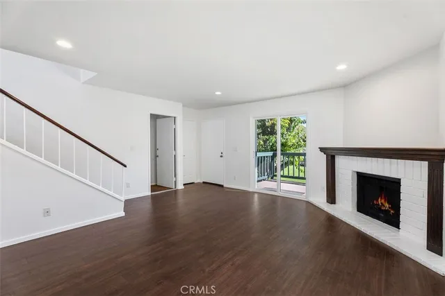 a view of an empty room with wooden floor fireplace and a window