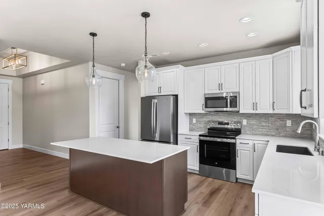 a kitchen with stainless steel appliances a stove a sink a refrigerator a center island a stove and white cabinets with wooden floor