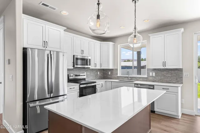 a kitchen with stainless steel appliances granite countertop a refrigerator a sink dishwasher a stove and white cabinets with wooden floor